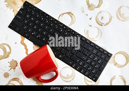 Tasse de café rouge renversée sur un clavier d'ordinateur sur une table avec des taches de café. Clavier rempli de boisson au café Banque D'Images