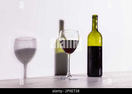 Un verre de vin et une bouteille jettent une longue ombre du soleil du soir. Banque D'Images