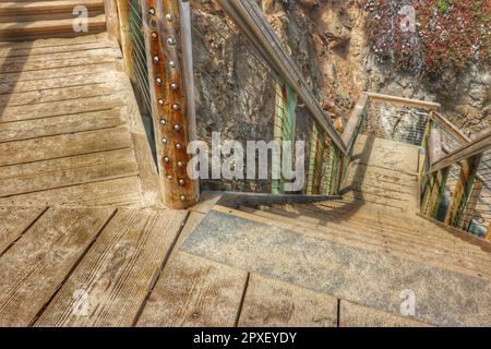 Un escalier en bois avec des mains courantes en métal menant à une falaise imposante Banque D'Images