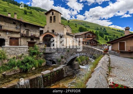 Vue sur la petite ville avec de vieilles maisons, église paroissiale et pont médiéval sur la crique alpine comme montagnes sur fond à Chianale, Italie. Banque D'Images