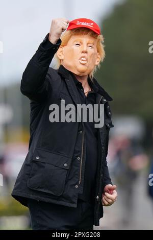 Une personne portant un masque de l'ancien président américain Donald Trump (au centre) au parcours de golf de Turnberry, dans le sud de l'Ayrshire, lors de la visite de l'ancien président américain au Royaume-Uni. Date de la photo: Mardi 2 mai 2023. Banque D'Images