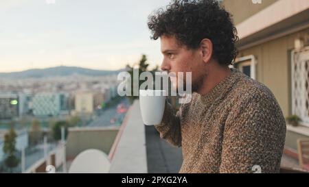 Un homme paisible donne sur la ville depuis le balcon et prend un café, bénéficie d'une vue magnifique Banque D'Images