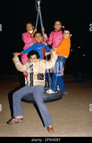 Arabie Saoudite Portrait des enfants dans le terrain de jeu de nuit jouant sur une balançoire à pneus Banque D'Images