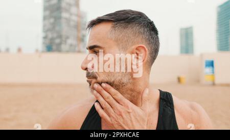 Gros plan d'un homme mature qui étire ses muscles du cou tout en se tenant sur la plage le matin Banque D'Images