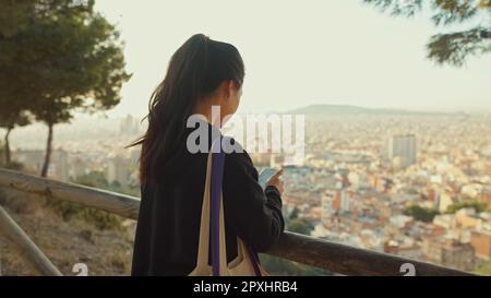 Une jeune femme se tient sur une plate-forme de visualisation avec un téléphone portable dans ses mains et regarde autour et regarde autour, vue arrière Banque D'Images