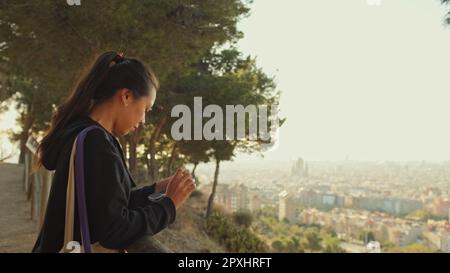 Une jeune femme se tient sur une plate-forme de visualisation avec un téléphone portable dans ses mains et regarde autour et regarde autour Banque D'Images