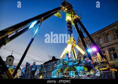 Frissons de foire, avec des gens hissés haut sur un bras de grue et tournés autour. Promenade nocturne à sensations fortes sur le terrain de foire. Angleterre Royaume-Uni Banque D'Images