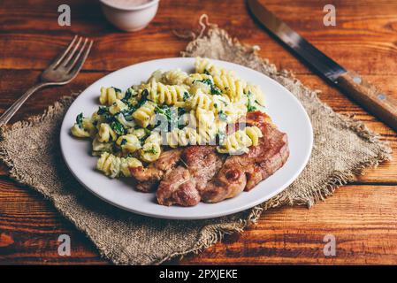 Steak de porc et pâtes crémeuses aux épinards et au thym Garni de parmesan râpé sur plaque blanche Banque D'Images