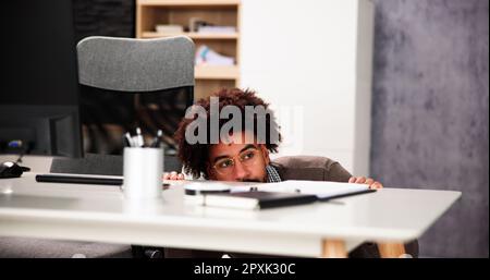 Un homme effrayé se cache derrière le bureau dans la chambre Banque D'Images