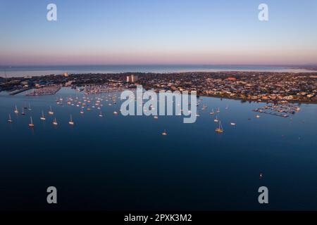 Vue aérienne d'une marina tranquille avec une variété de voiliers et de yachts illuminés par la lumière chaude du lever du soleil Banque D'Images