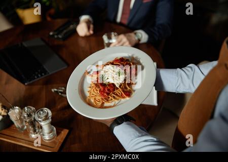 Gros plan du serveur tenant une assiette avec des pâtes et servant au client dans le restaurant Banque D'Images