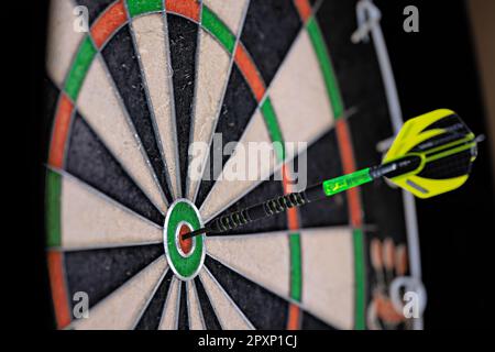 Un seul dart noir et vert collé dans le logo de la cible d'un dartboard. Gros plan sur un plan de travail. Banque D'Images