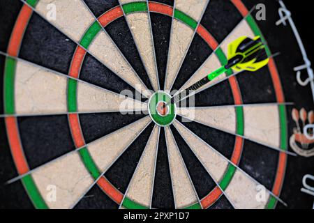 Un seul dart noir et vert collé dans le logo de la cible d'un dartboard. Gros plan sur un plan de travail. Banque D'Images