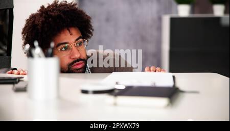 Un homme effrayé se cache derrière le bureau dans la chambre Banque D'Images