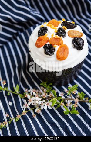 Le gâteau de Pâques, décoré d'abricots et de pruneaux séchés, se dresse sur un tablier bleu rayé, une branche fleurie. Concept de vacances religieuses de Pâques Banque D'Images