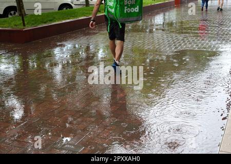 Un livreur de nourriture de la société Bolt marchant dans la bruine après une forte pluie sur un trottoir pavé à Bucarest, Roumanie sur 28 mai 2022 Banque D'Images