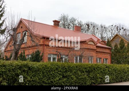 Une maison en briques rouges avec un toit rouge et des arbres avec des nids d'oiseaux en arrière-plan Banque D'Images