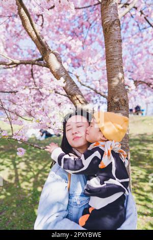 Un mon avec son enfant debout sous les arbres Sakura pendant la saison des cerisiers en fleurs. Banque D'Images