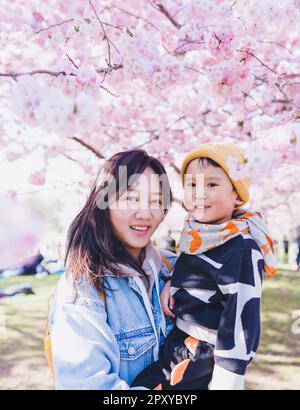 Un mon avec son enfant debout sous les arbres Sakura pendant la saison des cerisiers en fleurs. Banque D'Images