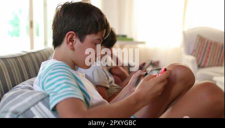 Enfants jouant à des jeux vidéo sur le canapé de la maison. Enfants regardant l'écran à l'aide d'appareils de jeu Banque D'Images