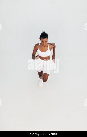 Prise de vue d'une jeune femme en train de courir dans un studio blanc en plein air. Angle élevé d'une sprint femelle mince. Banque D'Images