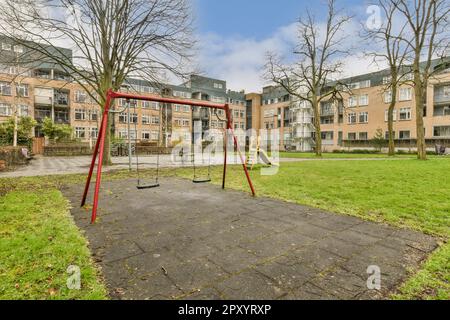 un terrain de jeu vide au milieu d'un quartier résidentiel avec des arbres et des bâtiments de chaque côté, il y a une balançoire rouge Banque D'Images