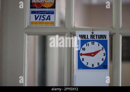 L'horloge « VA REVENIR » à la porte d'un bureau indique aux clients quand ils vont revenir. Parfois ils ne le font pas! Banque D'Images