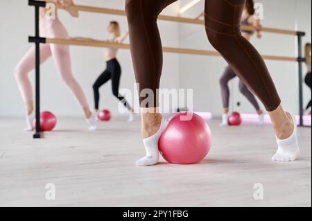 Vue en coupe basse de la rangée de femmes qui étirent les pieds à l'aide du ballon de fitness. Aérobic, pilates ou yoga au club de fitness féminin Banque D'Images