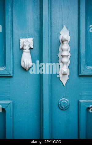 Un porte-outil en forme de main et une poignée en métal sur une ancienne porte peinte en bleu. Banque D'Images