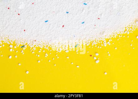 Poudre de lavage avec granules bleus et rouges sur fond jaune gros plan, vue de dessus. Banque D'Images