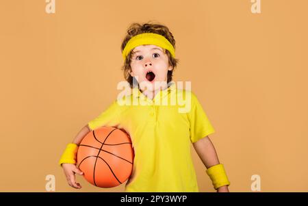 Surprise enfant garçon dans les vêtements de sport avec ballon de basket-ball. Petit ballon de base. Équipements sportifs. Jeu de basket-ball. Style de vie sportif actif. Enfance et Banque D'Images