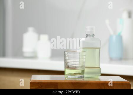 Bouteille et verre avec bain de bouche sur table en bois dans la salle de bains, espace pour le texte Banque D'Images