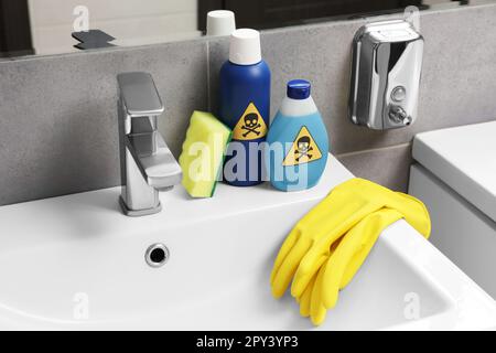 Bouteilles de produits chimiques domestiques toxiques avec panneaux d'avertissement, gants et éponge à récurer dans la salle de bains Banque D'Images