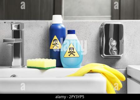 Bouteilles de produits chimiques domestiques toxiques avec panneaux d'avertissement, gants et éponge à récurer dans la salle de bains Banque D'Images