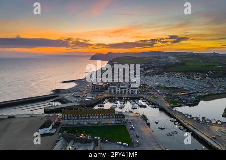 Vue depuis les airs tandis que le ciel brille d'orange au coucher du soleil au-dessus de la station balnéaire de West Bay sur la côte jurassique Dorset. Banque D'Images