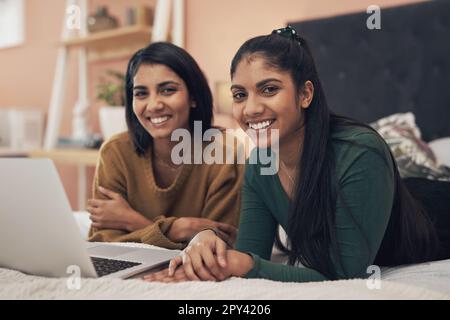 Nous trouvons toujours quelque chose pour nous divertir en ligne. deux jeunes femmes utilisant un ordinateur portable tout en étant couchée ensemble sur un lit. Banque D'Images