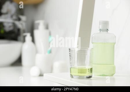 Bouteille de bain de bouche et verre sur étagère blanche dans la salle de bains, espace pour le texte Banque D'Images