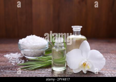 Huiles essentielles, fleur d'orchidée et sel de mer sur table en bois, gros plan Banque D'Images