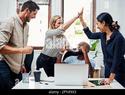 On dirait qu'ils ont battu la date limite. un groupe de collègues se réjouissent tout en se réunissant autour d'un ordinateur portable au bureau. Banque D'Images