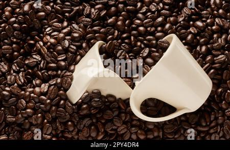 Êtes-vous dans l'humeur pour un cuppa ou deux. Gros plan de deux tasses sur une pile de grains de café. Banque D'Images