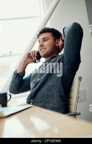 Conclure la vente par téléphone. un beau jeune homme d'affaires assis seul et utilisant son téléphone portable dans le bureau. Banque D'Images