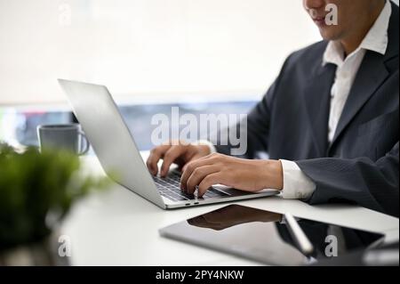 Image rapprochée d'un homme d'affaires asiatique du millénaire professionnel et concentré utilisant un ordinateur portable à son bureau. Banque D'Images