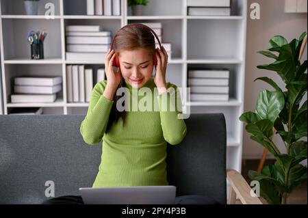 Décontractée femme asiatique millénaire aime écouter de la musique pendant son temps libre dans un salon. Concept de loisirs et de loisirs Banque D'Images