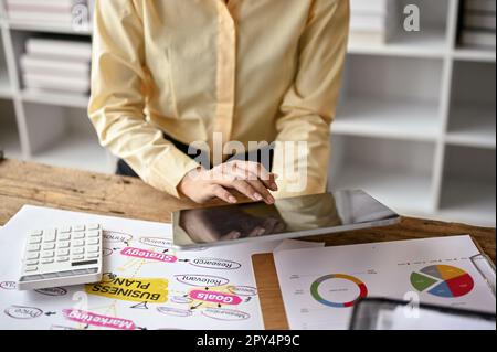 Image rognée et rapprochée d'une femme d'affaires professionnelle utilisant sa tablette numérique à son bureau. Banque D'Images
