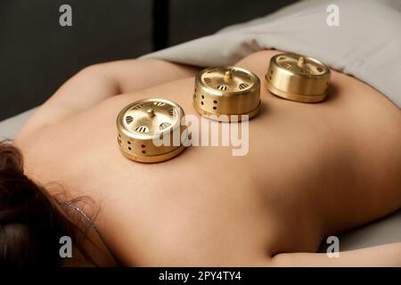 Traitement de la moxibution - les outils de médecine traditionnelle chinoise pour l'acupuncture points thérapie de chauffage. Boîte de brûleur en cuivre de moxibusse sur le dos de la femme Banque D'Images