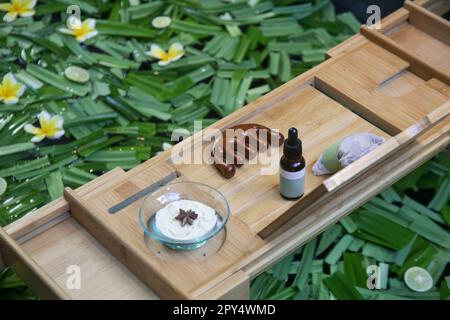 Baignoire pleine d'eau et d'herbes avec plateau de bain en bois avec divers produits cosmétiques, concept de détente et de bien-être de style de vie Banque D'Images