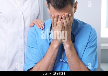 Médecin couvrant son visage avec les mains tandis que collègue le réconfortant à l'hôpital Banque D'Images