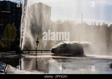 Göteborg, Suède - 01 mai 2022: Voitures traversant une rue remplie d'eau se laver soigneusement par une grande fuite d'eau de réseau Banque D'Images