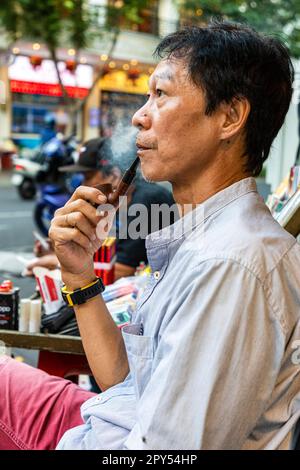 Homme vietnamien fumant pipe, assis au café de bord de route, Ho Chi Minh ville, Vietnam Banque D'Images