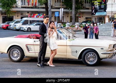 Mariée et marié posant avec 1967 Ford Mustang convertible utilisé comme voiture de mariage à l'extérieur de l'Opéra, Ho Chi Minh ville, Vietnam Banque D'Images